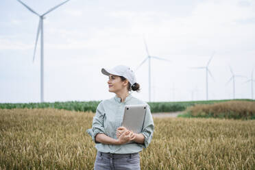 Smiling agronomist standing with laptop in front of wheat crops - EKGF00361