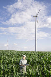 Farmer with laptop standing amidst plants at field on sunny day - EKGF00379