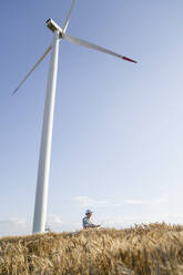 Agronom an einem sonnigen Tag unter einer Windkraftanlage - EKGF00389