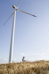 Agronomist standing under wind turbine on sunny day - EKGF00389