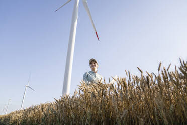 Glücklicher Agrarwissenschaftler inmitten von Weizenfeldern mit Windrädern im Hintergrund - EKGF00390