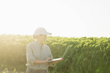 Landwirt mit Laptop auf einem Feld an einem sonnigen Tag - EKGF00402