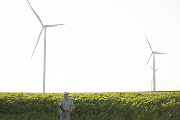 Farmer standing in front of plants and wind turbines - EKGF00406