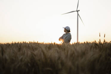 Landwirt in einem Weizenfeld mit Windrad bei Sonnenuntergang - EKGF00427