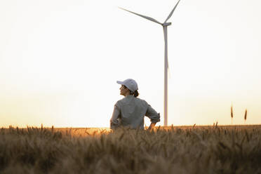Farmer standing in field with wind turbine in background - EKGF00428