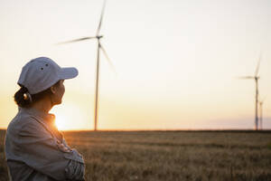 Landwirt mit Mütze betrachtet Windräder auf einem Feld - EKGF00433