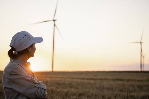 Farmer wearing cap looking at wind turbines in field - EKGF00433