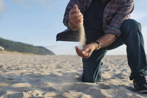 Älterer Mann hält Sand in der Hand am Strand - ASGF04081