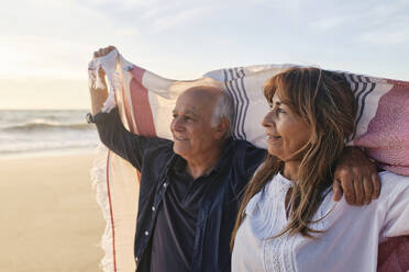 Glückliches älteres Paar mit Schal am Strand - ASGF04100