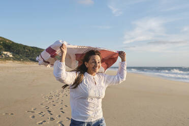 Happy senior woman with scarf at beach - ASGF04101