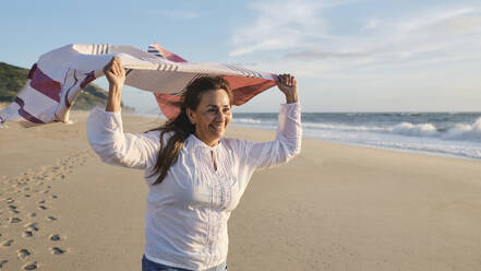 Happy senior woman with scarf at beach on sunny day - ASGF04102