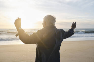 Älterer Mann mit erhobenen Armen vor dem Meer am Strand stehend - ASGF04114