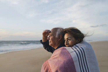 Smiling woman hugging man standing at beach - ASGF04123