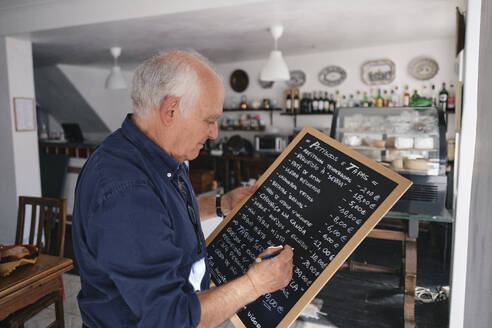 Cafebesitzer schreibt Speisekarte mit Stift auf schwarzes Brett - ASGF04159