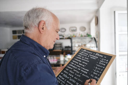 Älterer Café-Besitzer schreibt Speisekarte auf schwarzem Brett mit Stift - ASGF04160