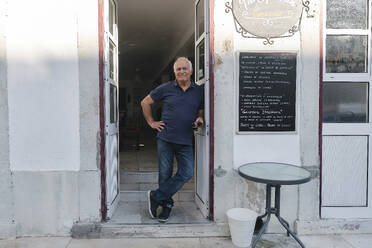 Smiling cafe owner standing in coffee shop doorway - ASGF04162