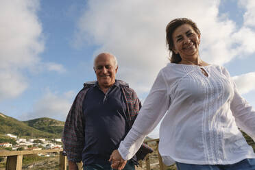 Happy couple holding hands and having fun under cloudy sky - ASGF04208