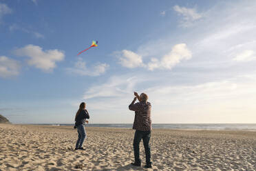 Älterer Mann und Frau fliegen Drachen am Strand an einem sonnigen Tag unter bewölktem Himmel - ASGF04216