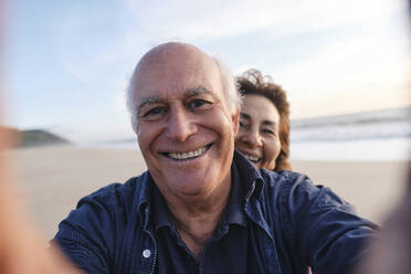 Älterer Mann und Frau fangen einen freudigen Moment ein, während sie ein Selfie am Strand machen - ASGF04221