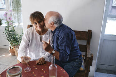Happy senior man kissing woman with glasses of wine in cafe - ASGF04245