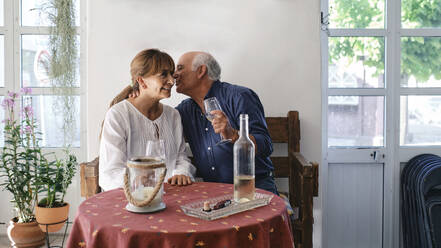 Glücklicher älterer Mann umarmt Frau im Restaurant sitzend - ASGF04248