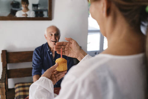 Glückliche ältere Frau überrascht Mann mit Cupcake im Café - ASGF04258