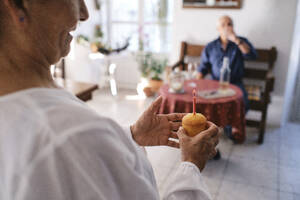 Glückliche ältere Frau hält Muffin mit Mann im Hintergrund - ASGF04262