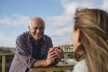 Smiling senior man holding coffee cup and looking at woman on sunny day - ASGF04270