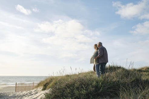 Älteres Paar steht zusammen inmitten von Pflanzen am Strand an einem sonnigen Tag - ASGF04280