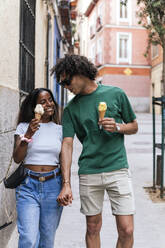 Lächelndes Paar, das eine Eistüte hält und auf der Straße spazieren geht - PBTF00089
