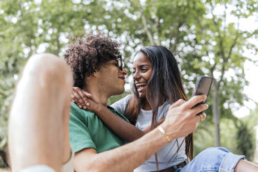 Lächelnde Freundin umarmt Freund mit Smartphone im Park - PBTF00094