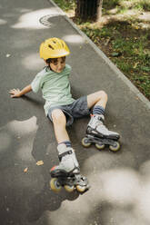 Upset boy wearing inline skates reclining on footpath - ANAF01831