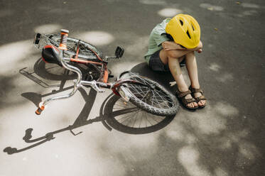 Verärgerter Junge sitzt neben dem Fahrrad auf dem Gehweg - ANAF01834
