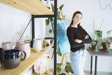 Artist with arms crossed standing near rack at workshop - YHF00008