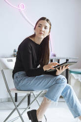 Nachdenklicher Künstler auf einem Stuhl sitzend mit einem Tablet-PC in einem Workshop - YHF00018