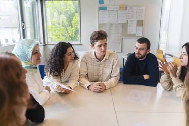 Schüler diskutieren am Tisch sitzend im Klassenzimmer - NJAF00456