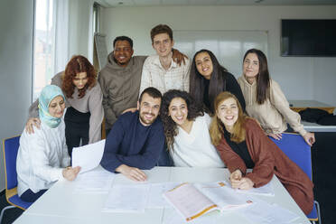 Zufriedene Schüler sitzen am Tisch im Klassenzimmer - NJAF00458