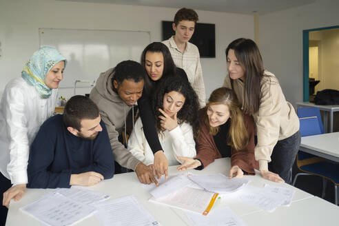 Schüler, die auf Papiere auf dem Tisch im Klassenzimmer zeigen - NJAF00461