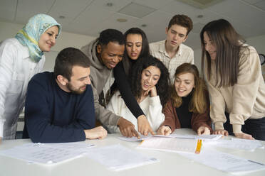 Multiethnische Schüler diskutieren über Notizen auf einem Tisch im Klassenzimmer - NJAF00462