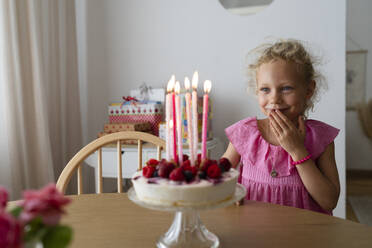 Lächelndes Mädchen steht hinter Kuchen mit Kerzen zu Hause - SVKF01547