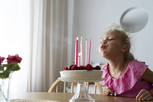 Blond girl blowing birthday candles at home - SVKF01548