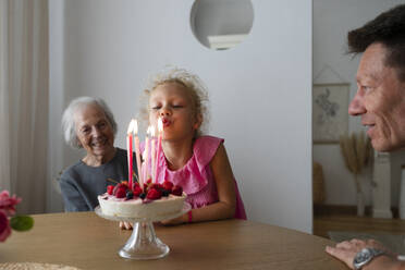Glückliches Mädchen bläst Geburtstagskerzen mit Familie zu Hause aus - SVKF01553