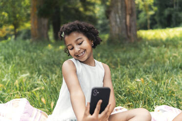 Eine fröhliche junge Frau hält einen Moment im Garten mit ihrem Smartphone fest und lächelt in die Kamera - PBTF00111