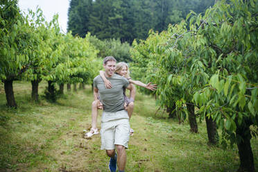 Smiling father giving piggyback ride to daughter in garden - NJAF00474