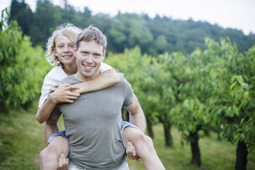 Smiling father giving piggyback ride to son in garden - NJAF00475