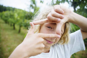 Blond boy showing finger frame sign in garden - NJAF00476