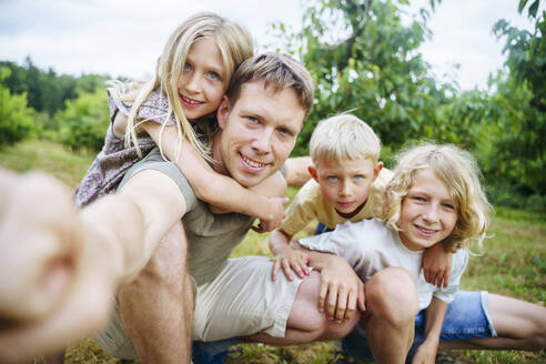 Ein Vater und seine Kinder fangen einen lustigen Moment ein, während sie ein Selfie in ihrem schönen Garten machen - NJAF00477