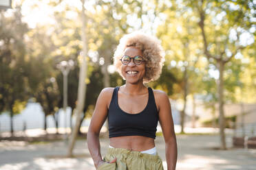 Positive young African American female basketball player in ethnic clothes and glasses looking at camera while standing on sports ground - ADSF45757