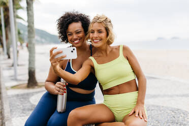 Zwei Fitness-Enthusiasten halten ihren glücklichen, gesunden Lebensstil mit der Kamera fest, während sie ein Strandtraining mit Blick auf den Ozean genießen - JLPSF30619