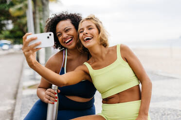 Fröhliche Frauen schließen sich bei einem Strandtraining zusammen und halten ihren aktiven und gesunden Lebensstil durch Selfies und Lachen fest - JLPSF30620